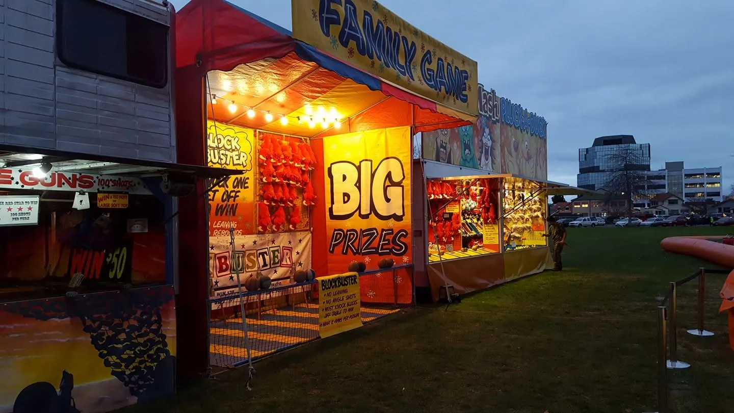 Lit-up game stalls with big prize signs at dusk