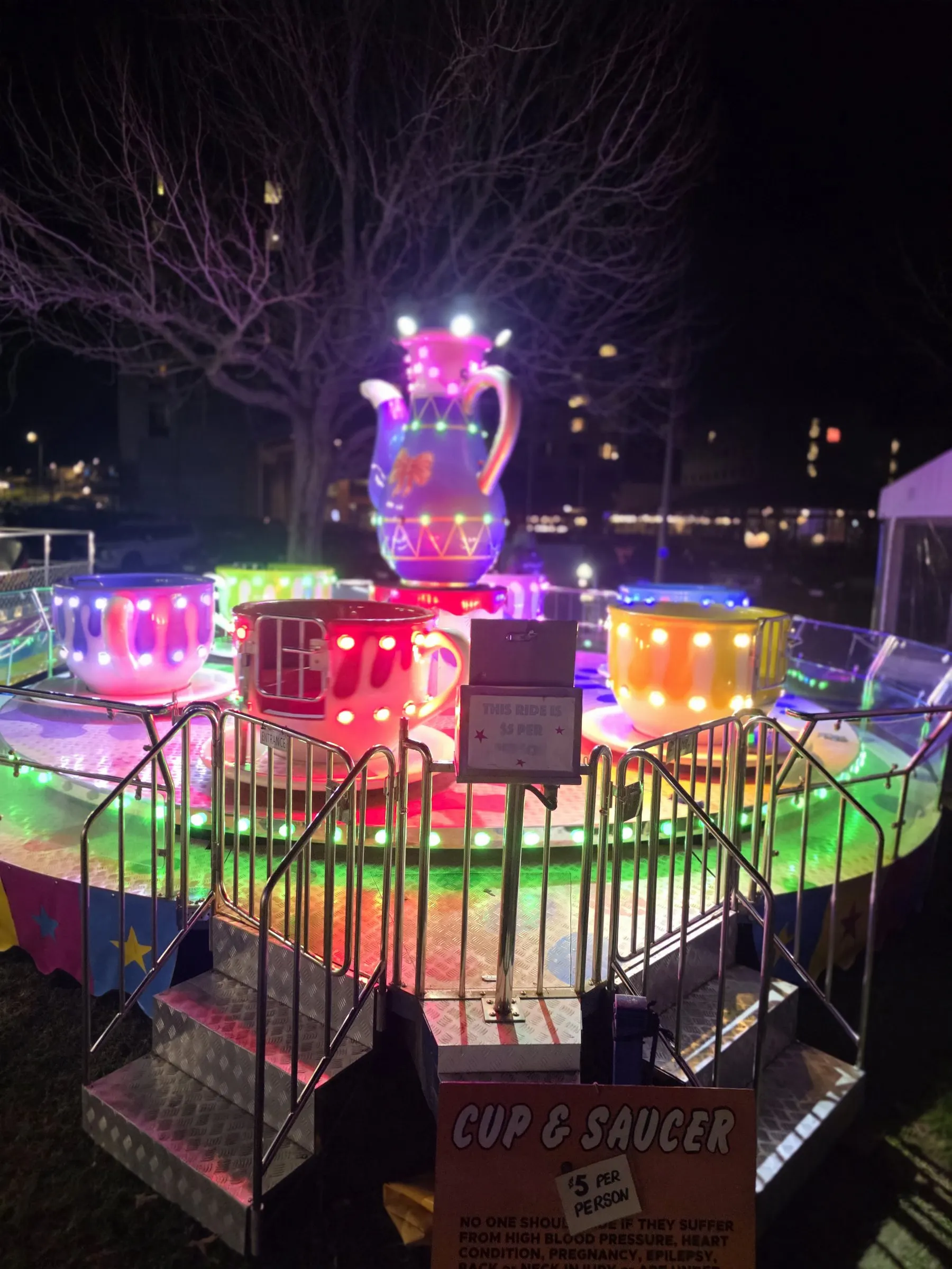 Teacup ride glowing pink and green at night with a giant teapot at its centre