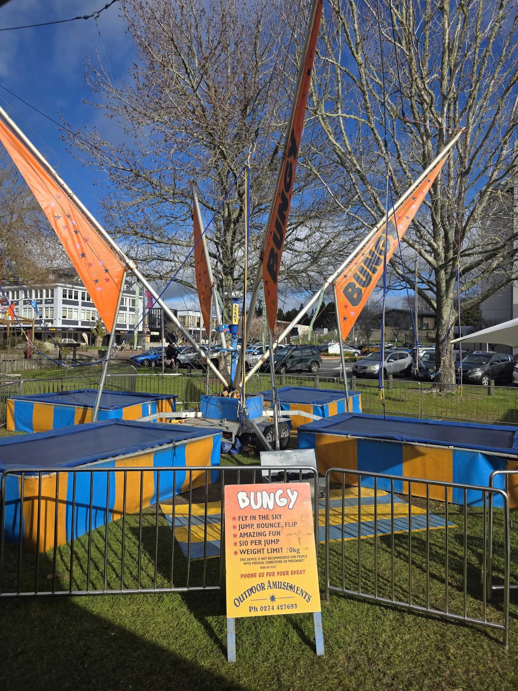 Bungy trampolines with orange flags and a bungy sign on a park lawn
