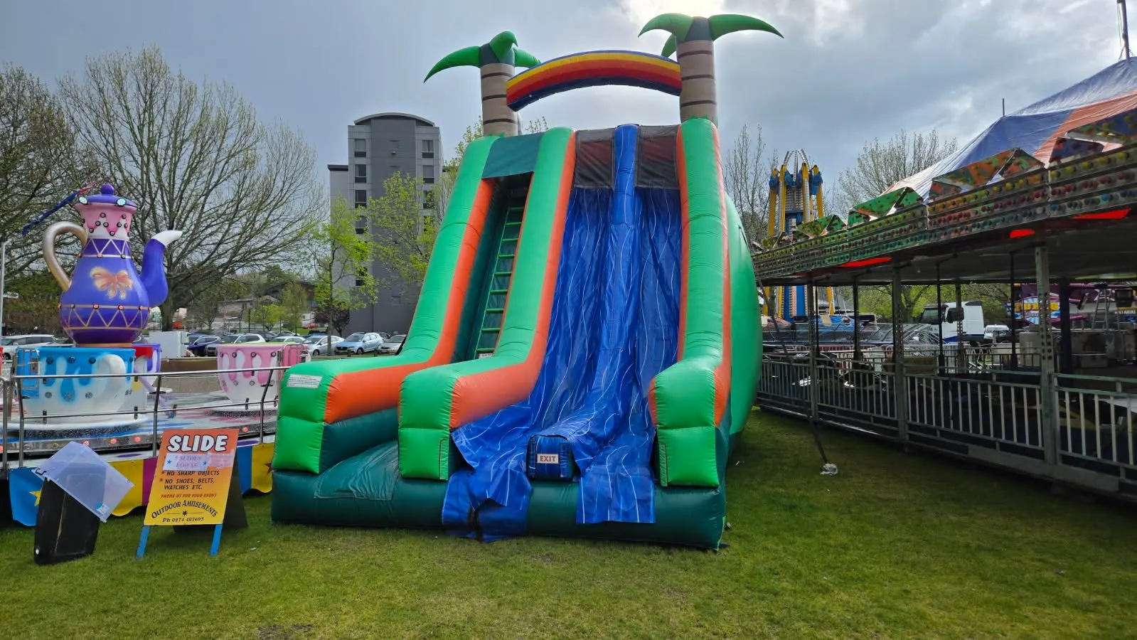 Green and blue inflatable slide with a rainbow arch and palm trees