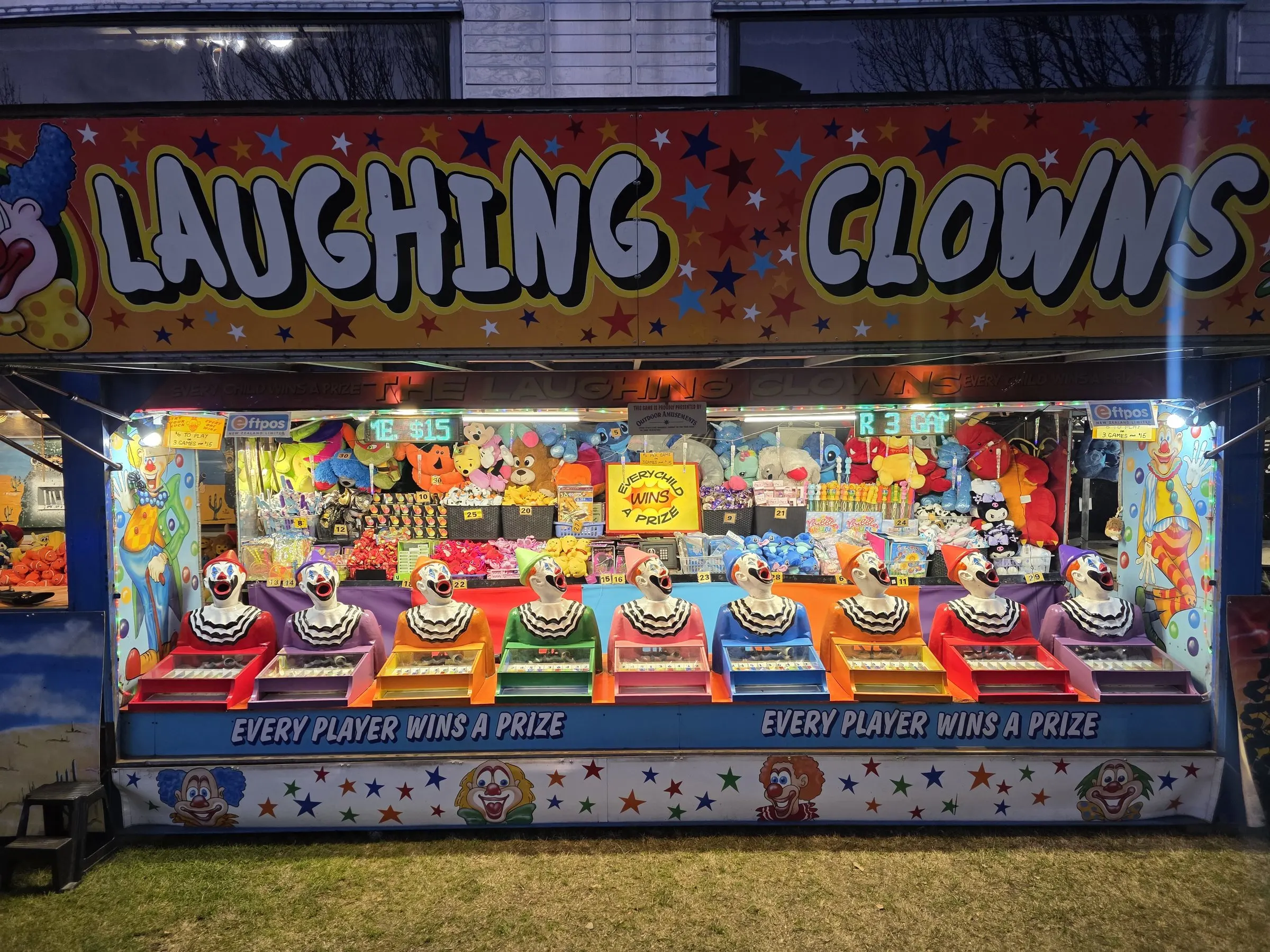 Laughing Clowns stall lit up at night with a row of clown heads