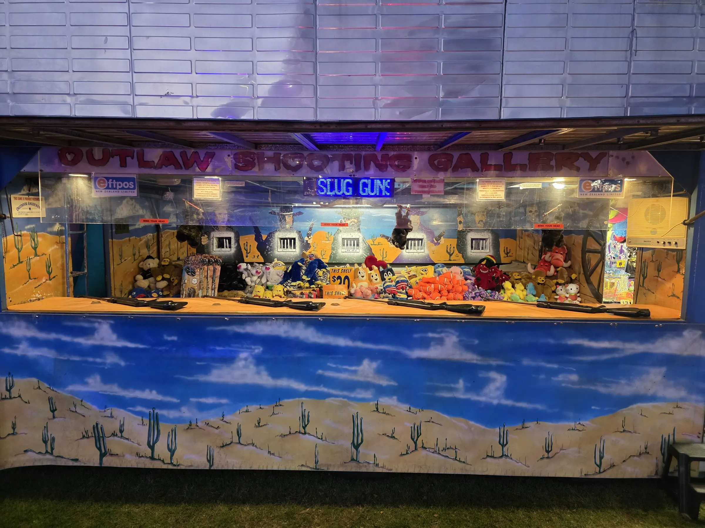 Outlaw Shooting Gallery stall with a desert backdrop and a slug guns sign