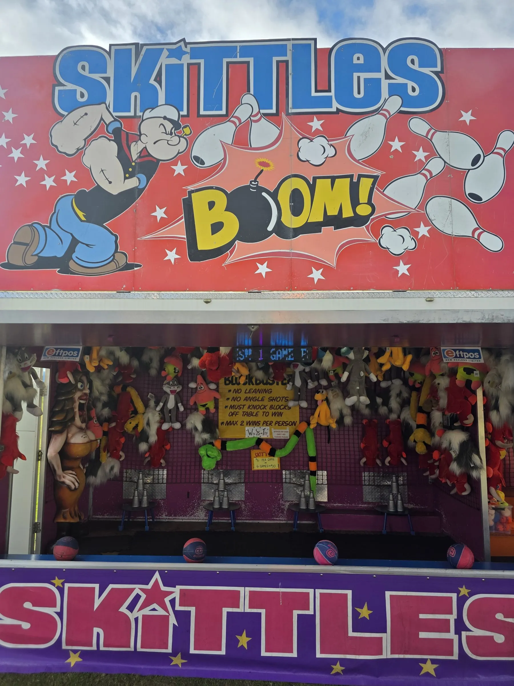 Skittles stall with a bright sign and rows of soft toy prizes