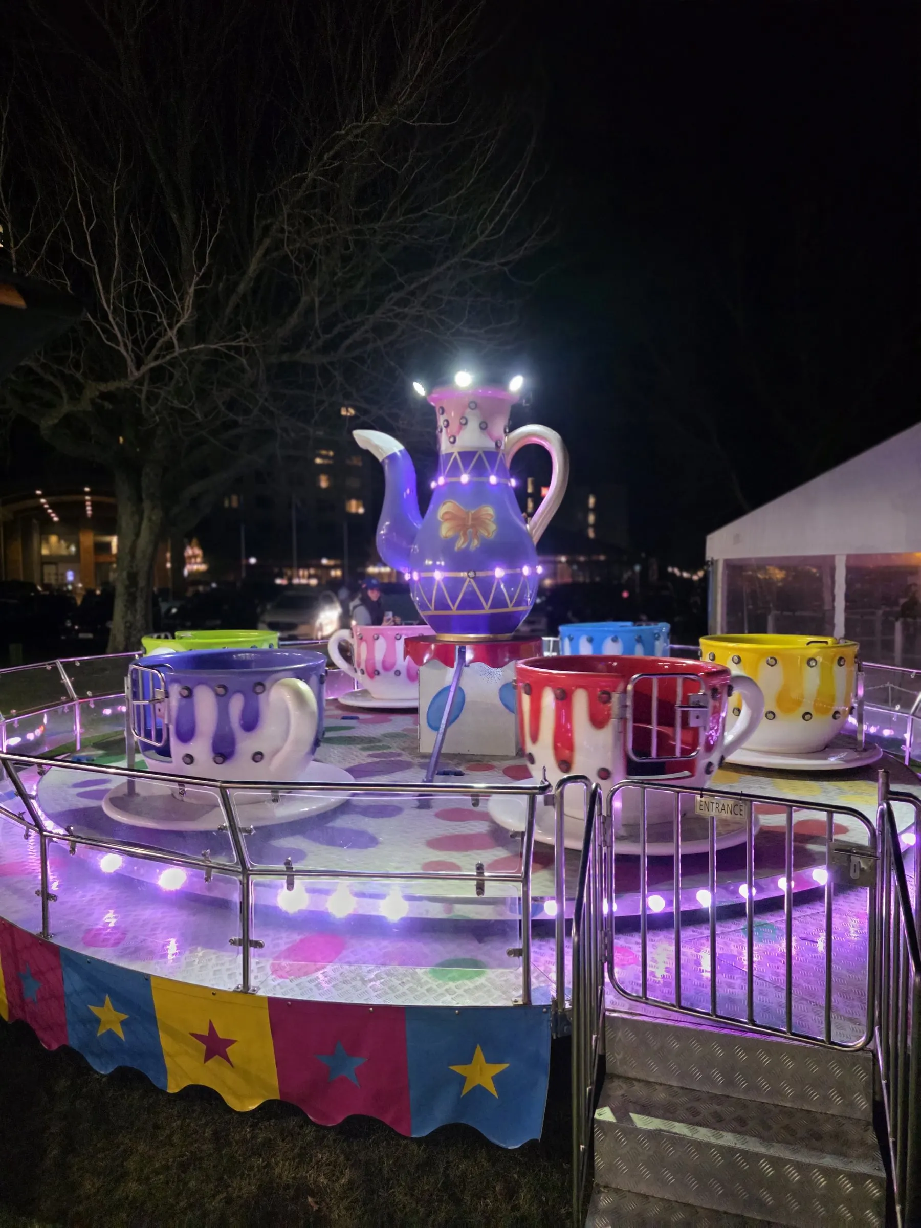 Teacup ride glowing purple at night with a giant teapot