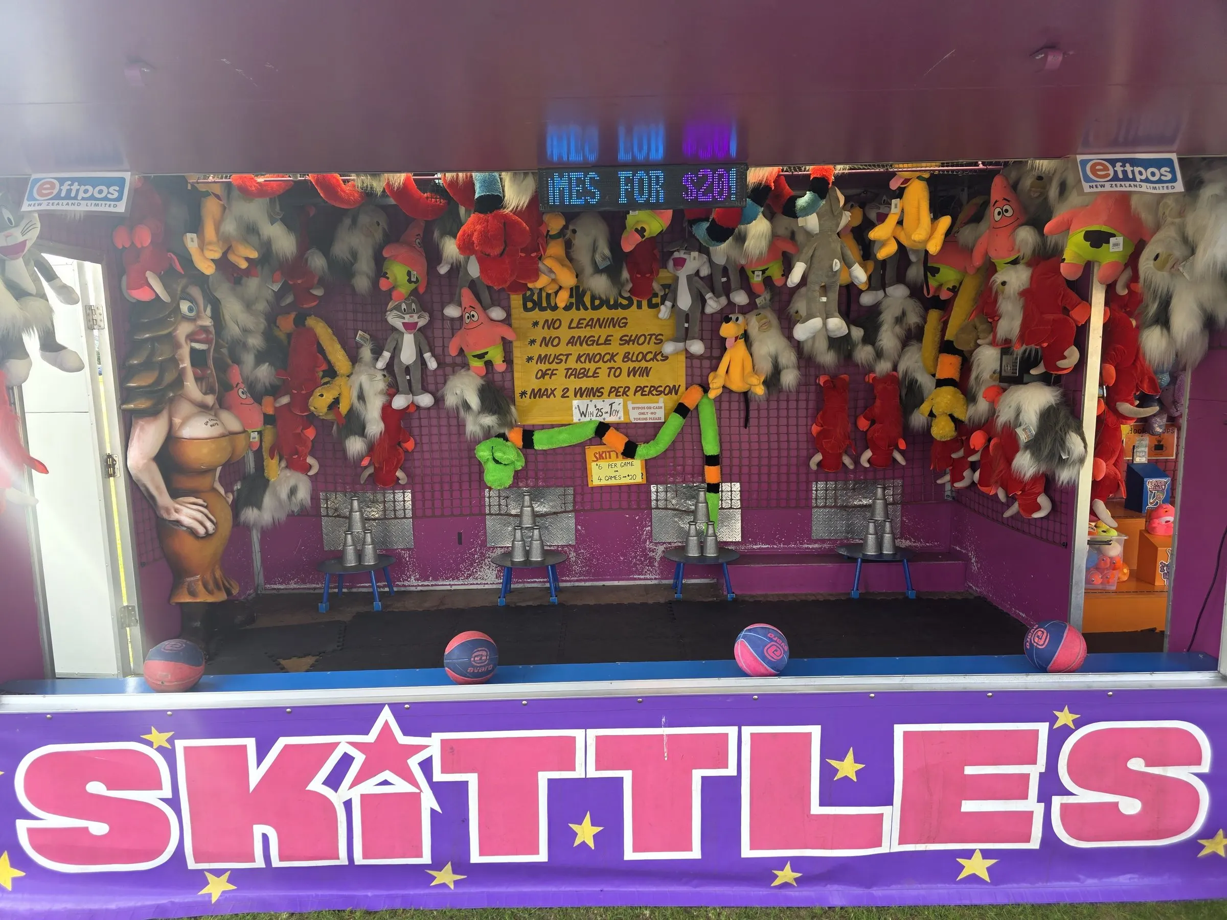 Skittles stall packed with soft toy prizes and a pink sign