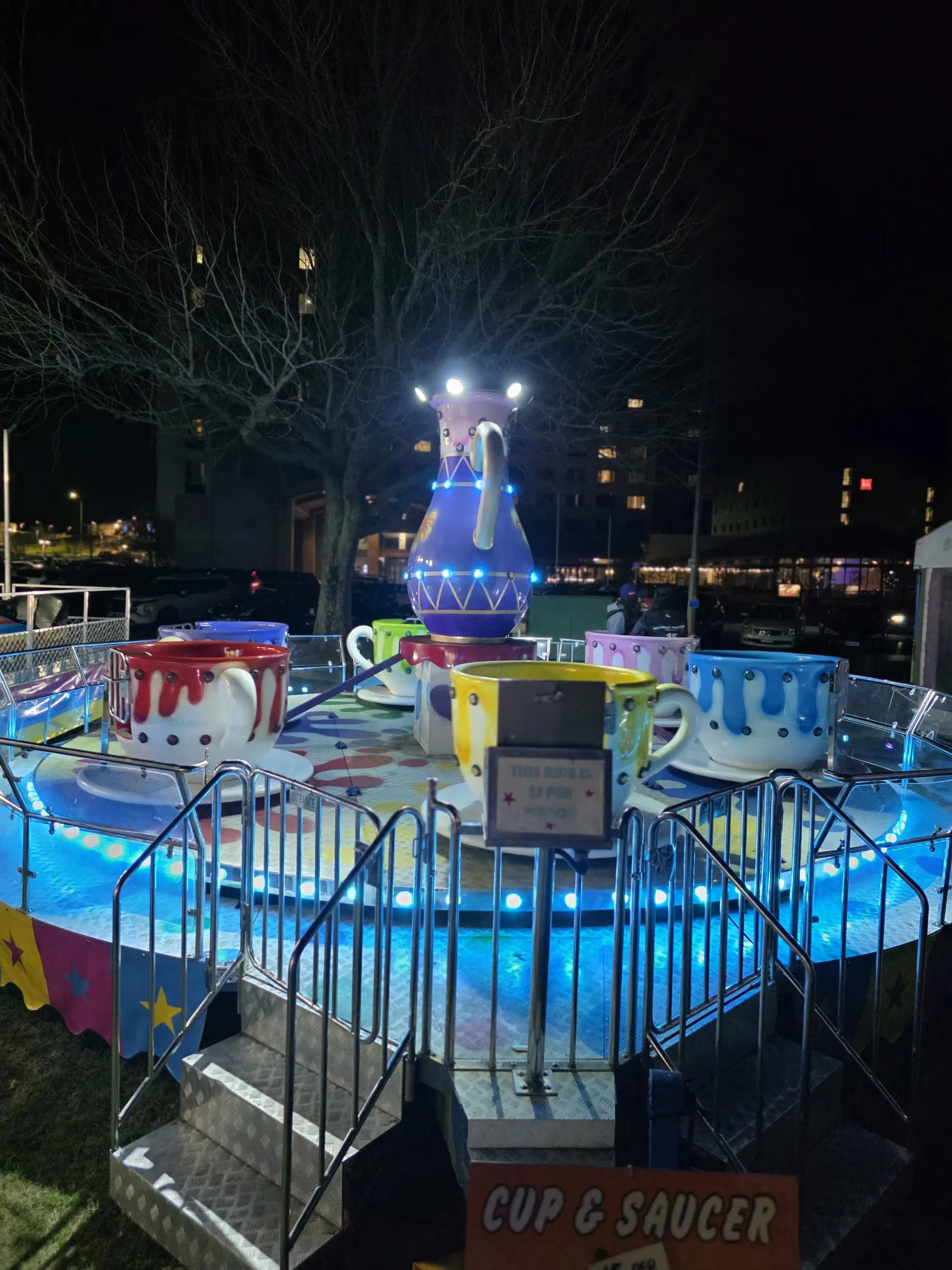 Teacup ride glowing blue at night with a giant teapot