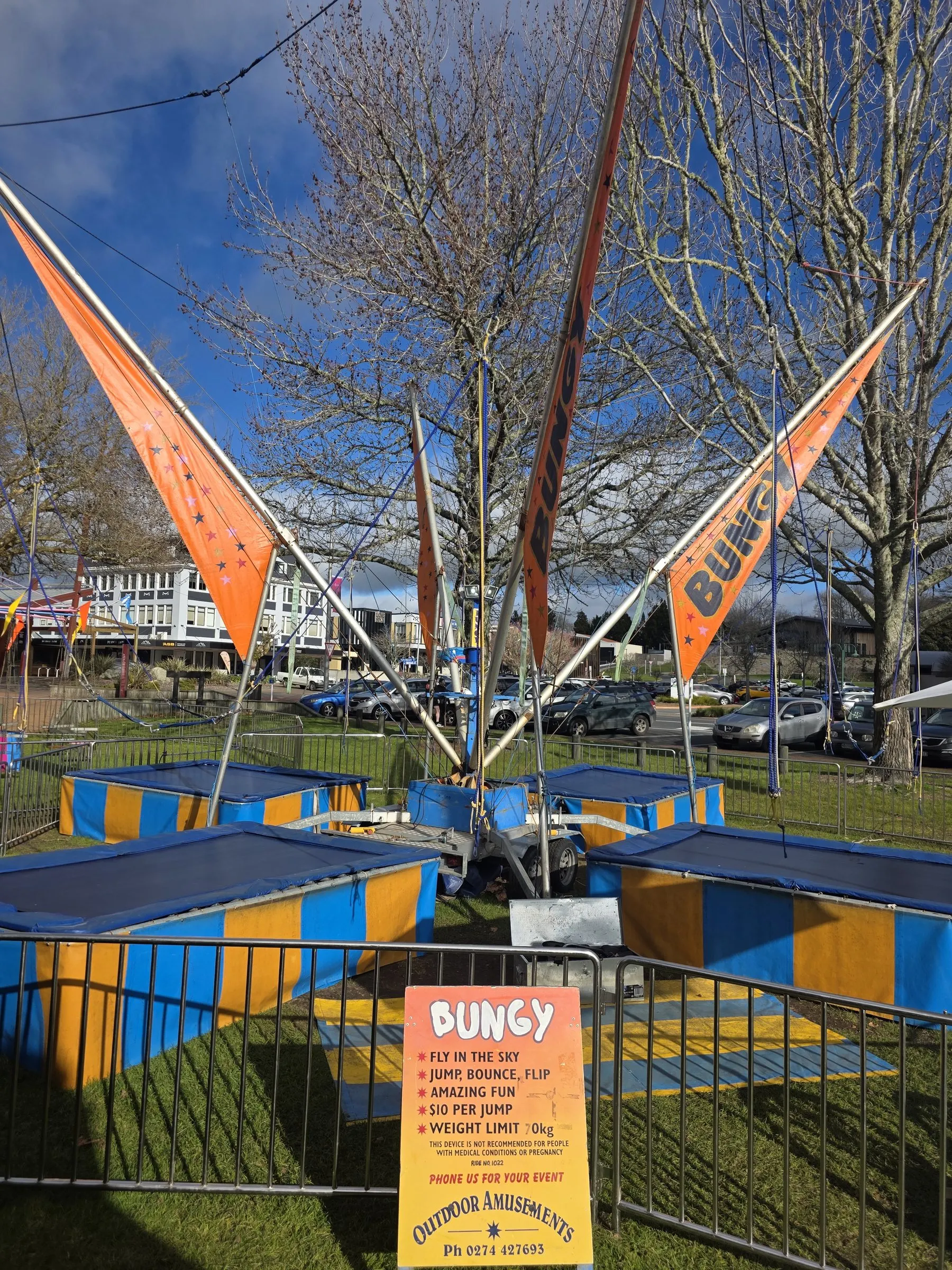 Bungy trampolines with orange flags and a bungy sign under a blue sky