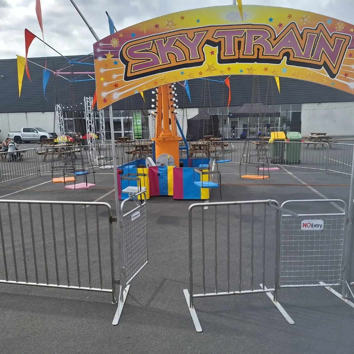 Sky Train swing ride behind safety barriers with a colourful arch