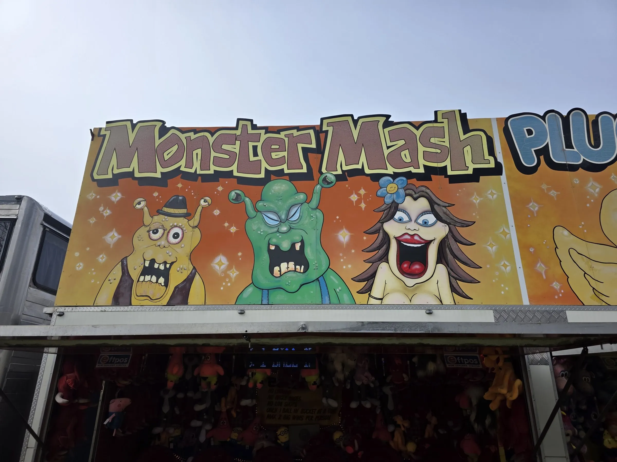 Monster Mash stall with a painted sign of green and orange monsters next to a Pluck a Duck sign